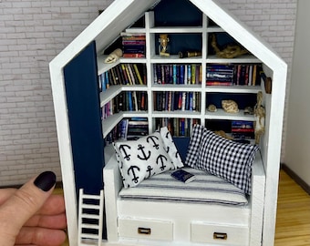 May include: A miniature white wooden house with a blue interior, featuring a built-in bookshelf, a small couch with pillows, and a ladder. The bookshelf is filled with miniature books and the couch has a striped cushion and a book on it.