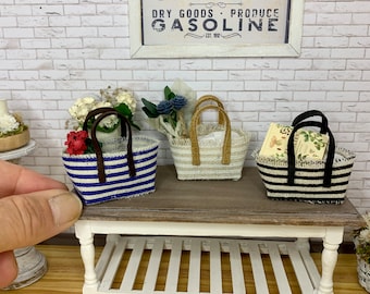 Könnte beinhalten: Drei kleine geflochtene Körbe mit Henkeln. Der linke Korb hat blaue und weiße Streifen mit roten Blumen. Der mittlere Korb ist beige mit weißen Streifen und blauen Blumen. Der rechte Korb hat schwarze und weiße Streifen mit einer Blumenkarte.