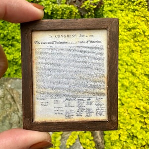 May include: A framed copy of the Declaration of Independence, printed on aged paper with faded ink. The document is surrounded by a dark brown wooden frame. The text reads "In CONGRESS, July 4, 1776. The unanimous Declaration of the thirteen united States of America."