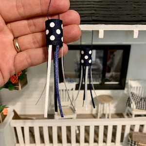 May include: Two miniature blue and white polka dot ribbon windsocks hanging from a white porch roof. The windsocks have white and blue ribbons hanging from the bottom.