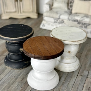 May include: Three miniature wooden pedestal tables. One table has a black top, one has a white top, and one has a brown top. The tables are on a wood floor.