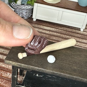 May include: A miniature wooden baseball bat and brown leather baseball glove with a white baseball on a dark brown wooden surface.