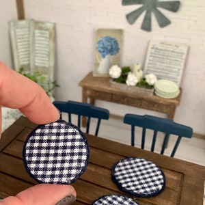 May include: Three round blue and white gingham chair pads with a dark blue trim. The pads are on a wooden table.