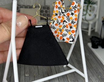 May include: A white clothing rack with two garments hanging on it. The garment on the left is a black skirt. The garment on the right is a sleeveless top with a white background and orange and black floral print.