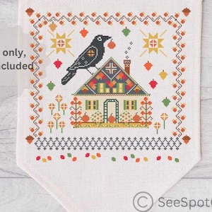 Peut inclure: Une bannière en tissu blanc avec un motif de point de croix représentant un corbeau noir perché sur une maison colorée. La bannière comprend le texte "For inspiration only, only pattern is included."
