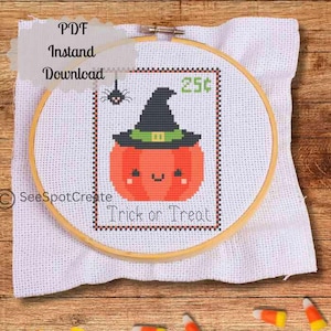 May include: A cross-stitch design featuring a smiling pumpkin wearing a witch hat, with the text "Trick or Treat." The design is framed in a wooden embroidery hoop and set against a white fabric background. A small spider is above the pumpkin.