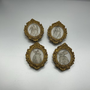 May include: Four small gold-framed pictures with images of white rabbits inside. The frames have ornate designs.