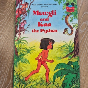 May include: A vintage Walt Disney Productions children's book titled Mowgli and Kaa the Python. The cover features a colourful illustration of Mowgli walking through a jungle with monkeys in the trees and Kaa the python hanging from a branch.