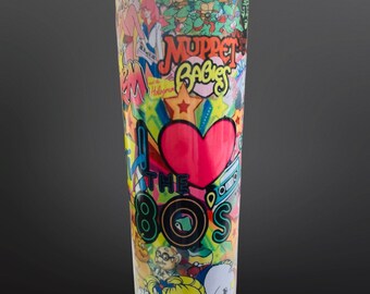 May include: A tall, insulated tumbler with a clear lid, covered in a collage of 1980s cartoon characters and phrases. The design includes the text "I ❤️ THE 80'S" with a large red heart, along with images of the Teenage Mutant Ninja Turtles and Muppet Babies.