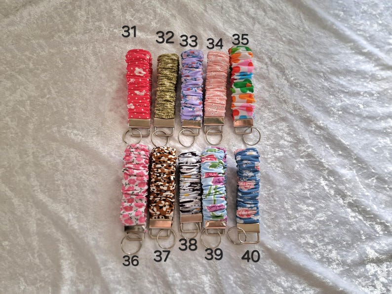 May include: Ten fabric-covered wristlet keychains arranged in two rows, numbered 31 through 40. Each keychain features a gathered, elasticized textile band in various patterns and colors, attached to a silver-toned metal clasp with a split ring.