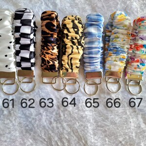 May include: Seven fabric wristlet keychains with metal hardware and split rings, numbered 61 through 67. Patterns include white with black dots, black and white checkerboard, leopard print, tiger stripes, blue gingham, blue floral, and a colorful floral print.