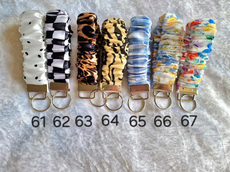May include: Seven fabric wristlet keychains with metal hardware and split rings, numbered 61 through 67. Patterns include white with black dots, black and white checkerboard, leopard print, tiger stripes, blue gingham, blue floral, and a colorful floral print.