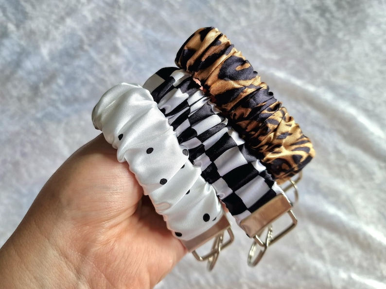 May include: Three fabric-covered keychains featuring a gathered, scrunchie-style design. One is white with black polka dots, one has a black and white checkered pattern, and the third features a brown and black leopard print. Each has a metal ring.