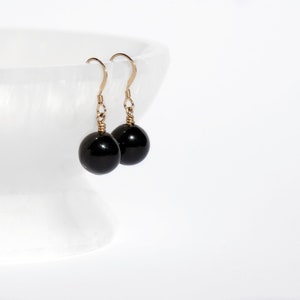 May include: A pair of black gemstone dangle earrings with gold-toned hooks.