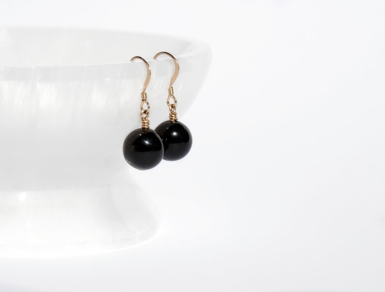 May include: A pair of black gemstone dangle earrings with gold-toned hooks.