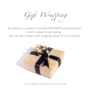 May include: A square gift box wrapped in light brown paper with a white star pattern, tied with a black satin ribbon and a gold metallic loop. The text reads: Gift Wrapping, All jewellery is placed in branded AIR+EARTH jewellery boxes, airandearthjewellery.etsy.com.