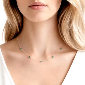 May include: A delicate silver chain necklace featuring five small, round, smooth green beads spaced evenly along the length of the chain. The necklace rests against the neck, showcasing a simple design with a metallic finish and green accents.