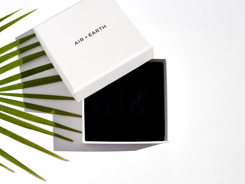 May include: A white box with the text "AIR + EARTH" on the lid. The box is open and the inside is lined with black velvet.