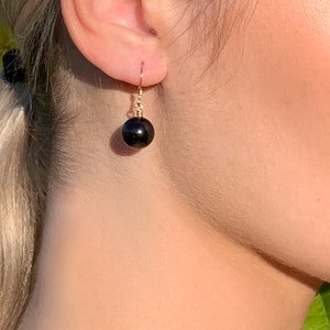 May include: A pair of gold earrings with a single black gemstone dangling from each earring.