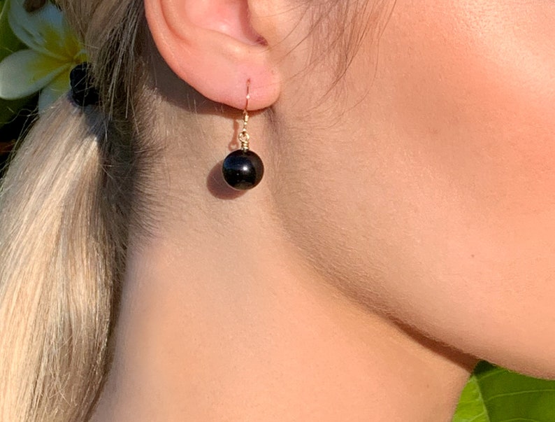 May include: A pair of gold earrings with a single black gemstone dangling from each earring.