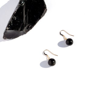 May include: A pair of gold earrings with black gemstone beads. The earrings are on a white background.