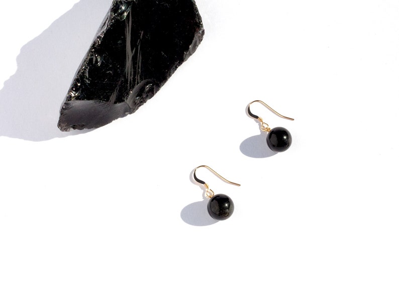 May include: A pair of gold earrings with black gemstone beads. The earrings are on a white background.