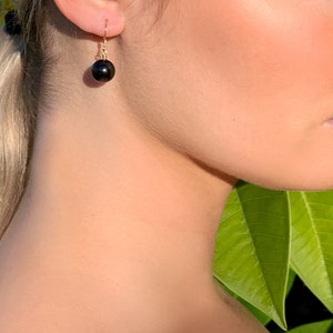 May include: A pair of gold dangle earrings with a black pearl drop.