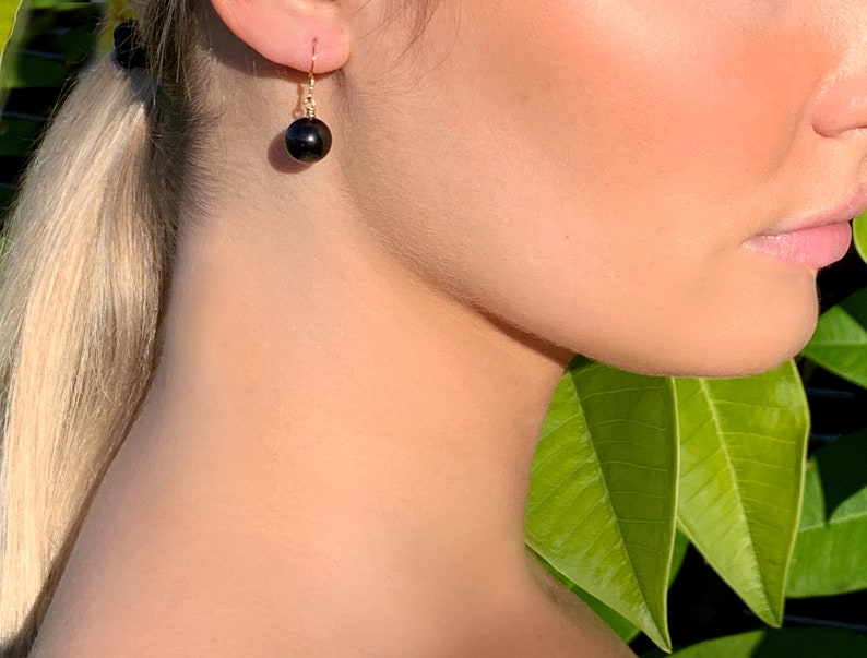 May include: A pair of gold dangle earrings with a black pearl drop.