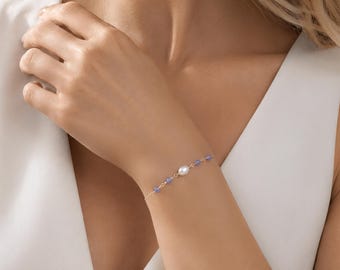 May include: A delicate gold chain bracelet featuring a single central white oval pearl flanked by small, round, light blue gemstone beads on each side. The bracelet is constructed with thin gold links connecting the pearl and the blue beads.