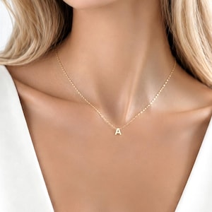May include: A delicate gold chain necklace featuring a small, centred pendant in the shape of the capital letter A. The necklace has a thin, reflective link chain that rests against the collarbone, providing a simple and clean aesthetic.
