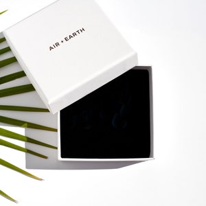 May include: A white box with the text "AIR + EARTH" on the lid. The box is open and the inside is lined with black velvet.