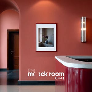 May include: A red-framed picture of a vase with flowers hangs on a red wall. A modern, red counter with a white top is in the foreground. The text "the mock room (psd)" is on the wall. A silver wall sconce is on the right.