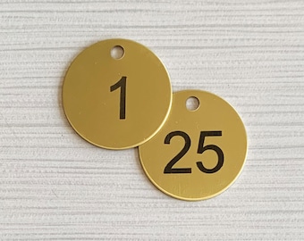May include: Two round, gold-coloured metal tags with black numbers. The tag on the left has the number "1" and the tag on the right has the number "25".