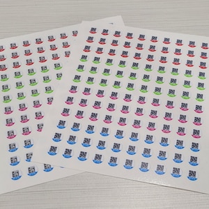 May include: Two sheets of stickers featuring a top hat design with a QR code. The hats are in red, green, pink, and blue, with a black QR code in the center. The stickers are on a white background.