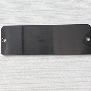May include: A silver rectangular metal plate with rounded corners and two small holes on each side.