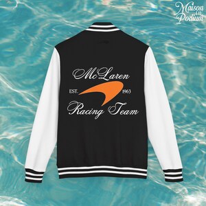 Può includere: Giacca college nera e bianca con il logo McLaren Racing Team sul retro. La giacca ha maniche bianche e un corpo nero con strisce bianche sul colletto, polsini e orlo. Il logo McLaren è arancione e bianco.