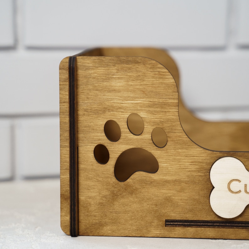 Peut inclure: Organisateur en bois marron clair pour nourriture et friandises pour animaux de compagnie. Il pr&eacute;sente une d&eacute;coupe en forme de patte et une &eacute;tiquette en forme d'os. Le mot "Cu" est visible sur l'&eacute;tiquette en forme d'os.