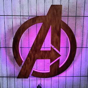May include: A dark brown wooden wall sign featuring the Avengers logo, which consists of a capital letter A enclosed within a circular frame. The sign is illuminated from behind with a vibrant purple LED light that glows around the edges.