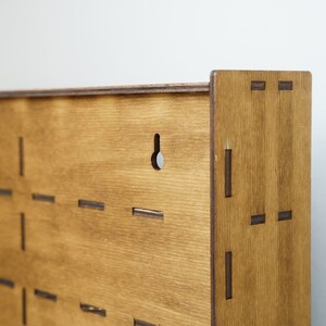 May include: A wooden wall organizer with a grid of slots for holding items. The organizer has a hole at the top for hanging. The wood is a light brown color.
