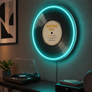 May include: A circular wall-mounted light fixture shaped like a vinyl record with a bright teal neon ring. The center label features the text RETRO PARTY and DAN ALL NIGHT in black and gold lettering against a white background with a thin black cord.