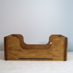 Peut inclure: Un organiseur de bureau en bois avec une finition marron chaud. L'organisateur a une base rectangulaire avec des d&eacute;coupes incurv&eacute;es sur les c&ocirc;t&eacute;s et une ouverture centrale. Le grain du bois est visible.