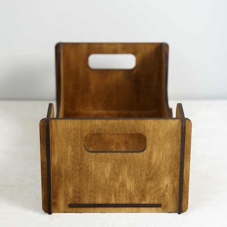 Peut inclure: Une caisse de rangement en bois avec une finition marron fonc&eacute;. La caisse a une forme rectangulaire avec un dos incurv&eacute; et deux d&eacute;coupes rectangulaires pour les poign&eacute;es &agrave; l'avant. Le grain du bois est visible, et la caisse semble vide.