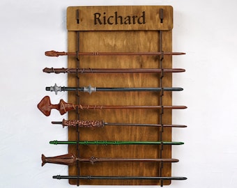 Puede incluir: Un soporte de varitas de madera para colgar en la pared con el nombre "Richard" grabado en la parte superior. El soporte tiene ocho ranuras para guardar varitas, y está lleno de varitas de varios colores.