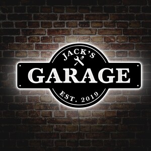 May include: Black and white metal sign with the text "Jack's Garage Est. 2019" and a wrench and screwdriver crossed in the center.