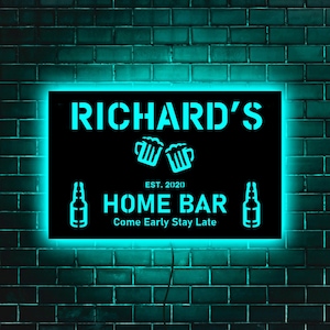 May include: Black neon sign with white text that reads "Richard's" with two beer mugs and the text "EST. 20(20) HOME BAR Come Early Stay Late".