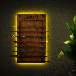 May include: A wooden wall-mounted wand holder with the name "Richard" engraved on it. The holder has eight slots for wands and is illuminated with a yellow light.