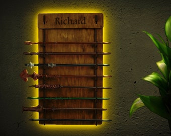 Puede incluir: Un soporte de varitas de madera para colgar en la pared con el nombre "Richard" grabado. El soporte tiene ocho ranuras para varitas y está iluminado con una luz amarilla.