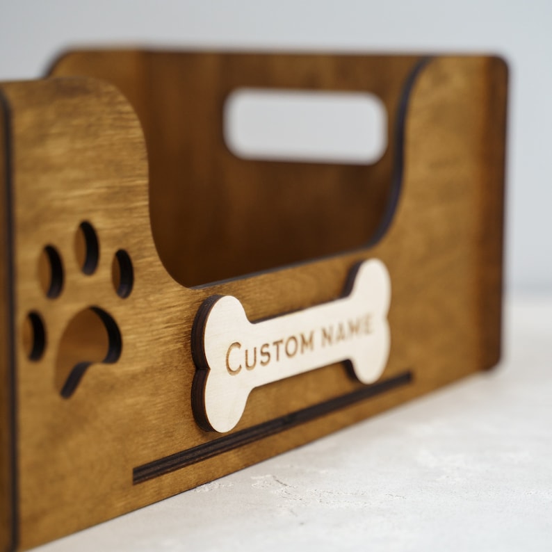 Peut inclure: Un organisateur en bois pour fournitures pour animaux de compagnie avec une poign&eacute;e et une d&eacute;coupe en forme de patte. Une &eacute;tiquette en forme d'os avec le texte "CUSTOM NAME" est attach&eacute;e &agrave; l'avant. L'organisateur est en bois teint&eacute;.