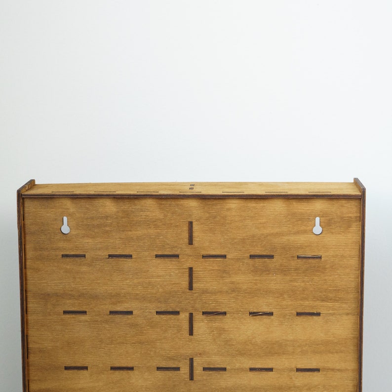 May include: A wooden wall-mounted shelf with a grid of slots for displaying items. The shelf has a light brown stain and two holes for hanging.