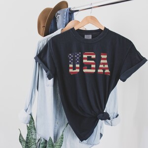 May include: A black t-shirt with a vintage-style American flag graphic that spells out "USA".